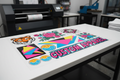 DTF gang sheet flat lay showing multiple colorful custom designs arranged on clear film transfer sheet
